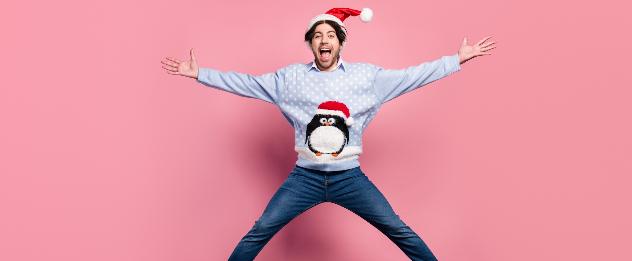 Mann mit Weihnachtsmütze und Pulli springt vor Freude in die Luft